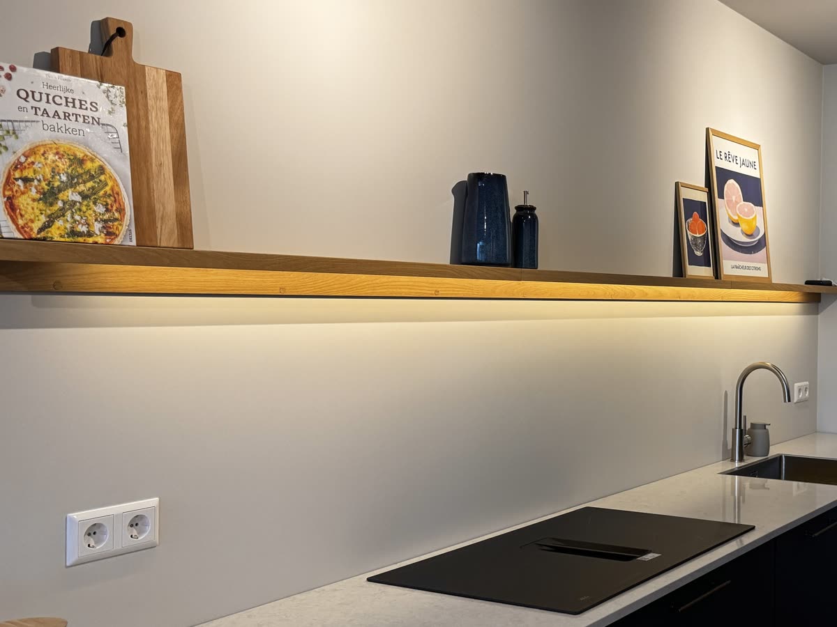 Een houten wandplank boven het aanrecht, met een ledstrip eronder die het werkblad verlicht