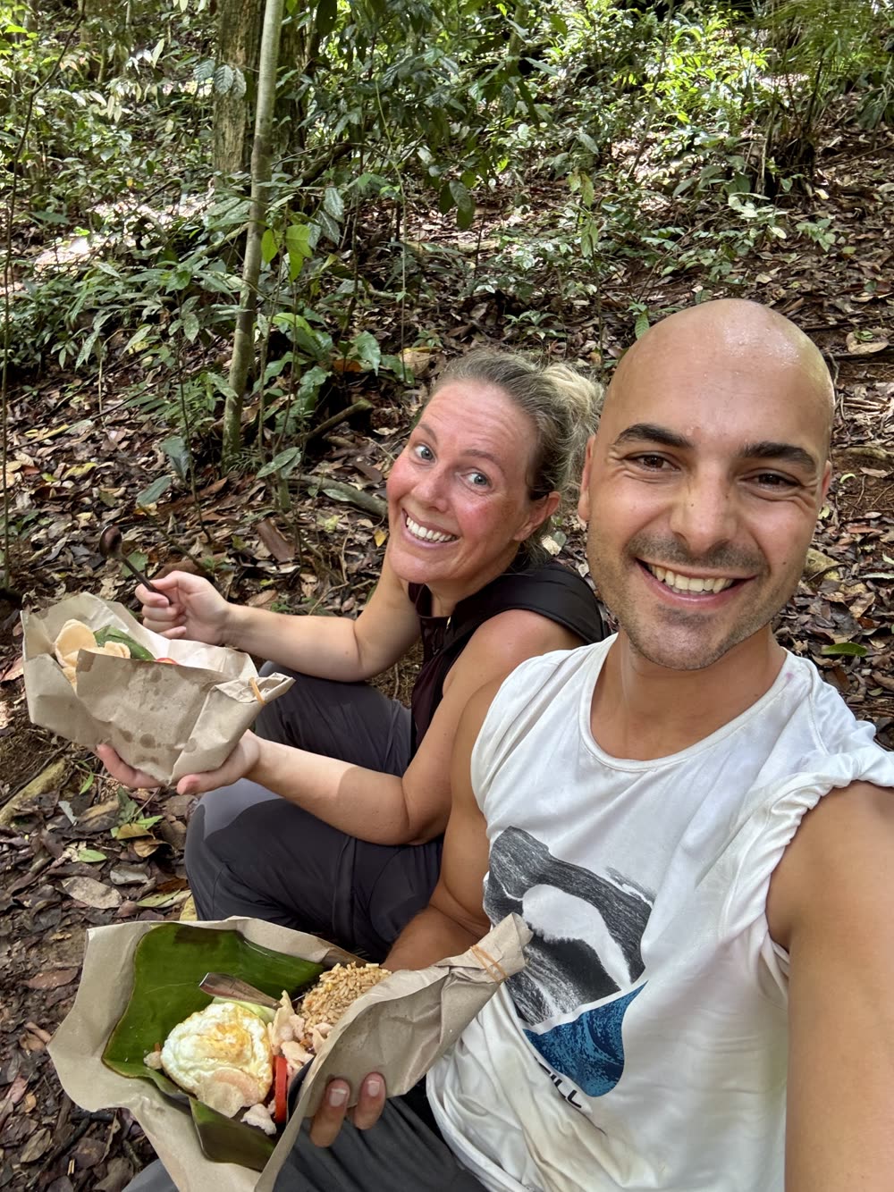 Jidde en Sharon lunchen lachend op de grond in een tropisch bos, tijdens een wandeling